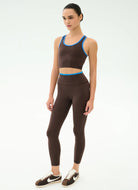 Woman wearing a brown sports bra and leggings set with blue trim on a white background