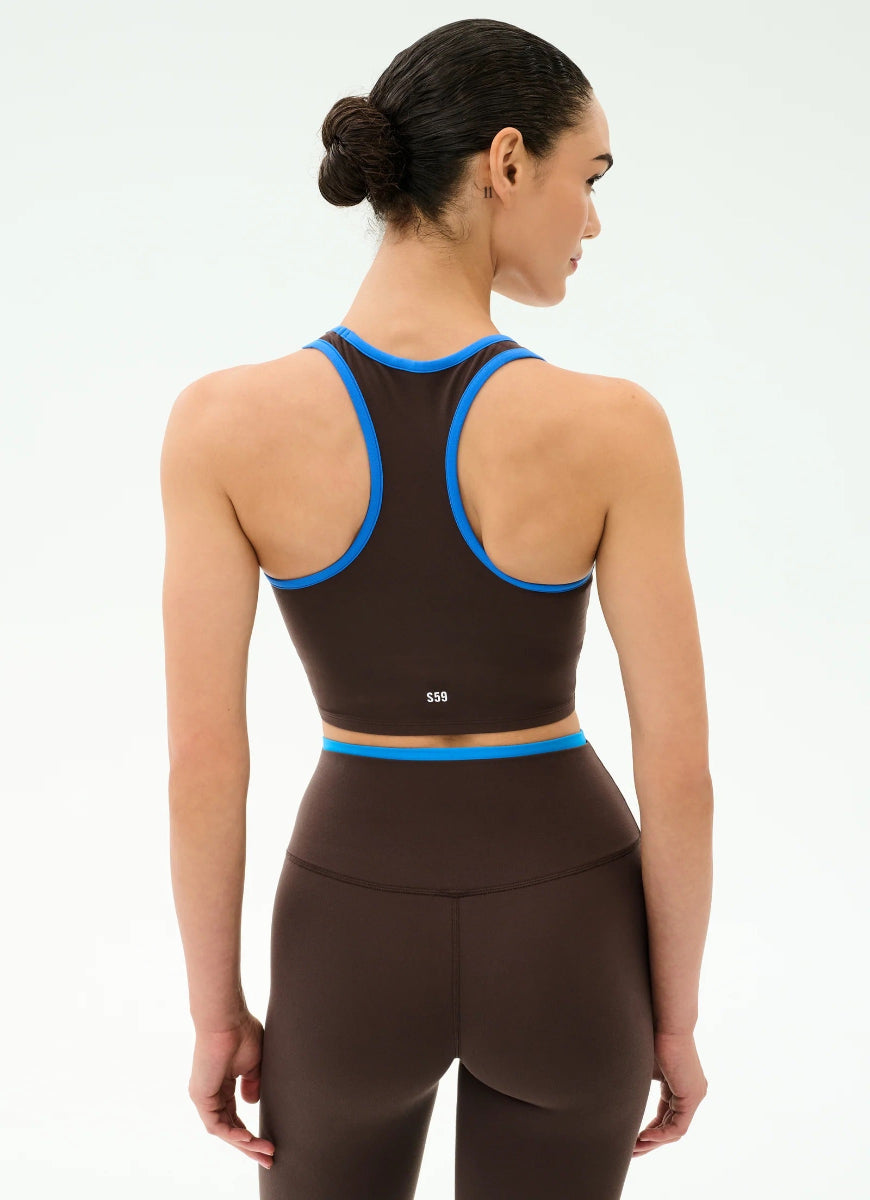 Woman wearing a brown sports bra and leggings with blue accents on a white background