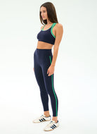 Woman wearing a navy sports bra and leggings with green accents on a white background
