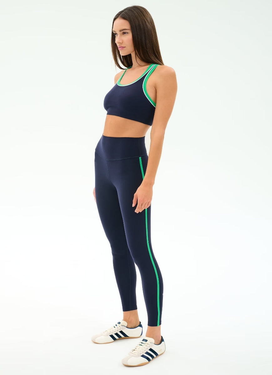 Woman wearing a navy sports bra and leggings with green accents on a white background