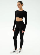 Person wearing a black long-sleeve crop top and leggings on a white background