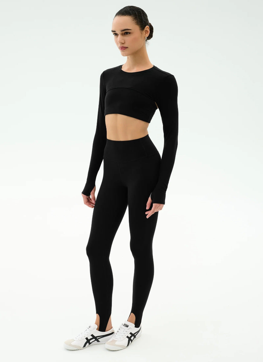 Person wearing a black long-sleeve crop top and leggings on a white background