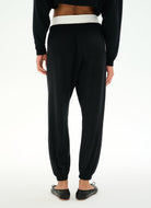 Black jogger pants with a contrasting white waistband, shown from the back on a model wearing a black crop top and black flats.