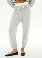 Light heather gray jogger pants with an elastic waistband, white drawstring, and elastic cuffs, shown on a model wearing black flats against a white background.
