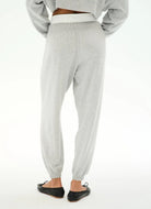 A person shown from the back wearing light heather gray jogger sweatpants with an elastic waistband and elastic ankle cuffs, paired with black flats against a plain white studio background.