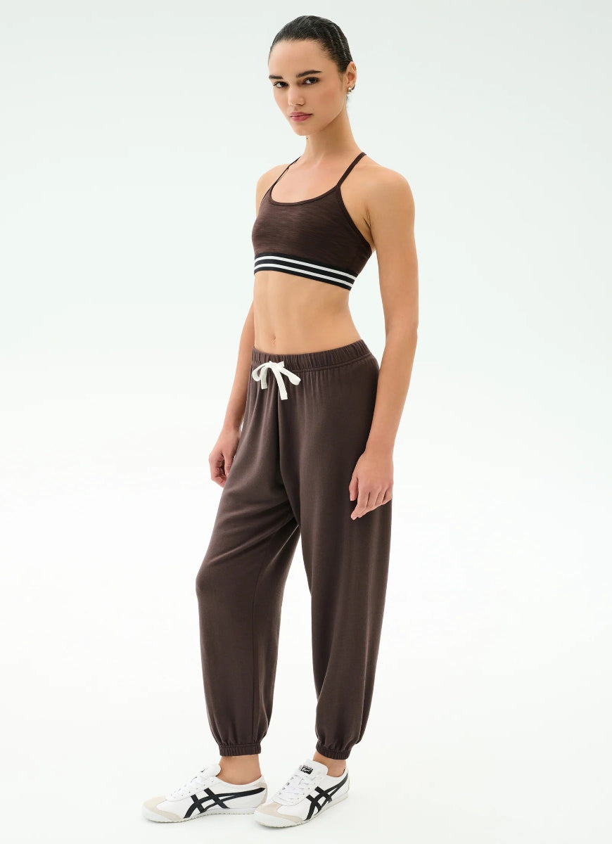 Woman wearing a brown sports bra and pants with white sneakers on a white background