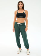 Woman wearing a black sports bra and green jogger pants on a white background