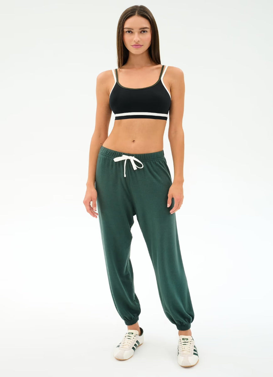 Woman wearing a black sports bra and green jogger pants on a white background