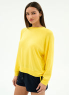 Woman wearing a yellow long-sleeve top and black shorts on a white background