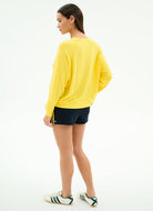 Person wearing a yellow long-sleeve shirt and black shorts on a white background