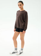 Person wearing a brown long-sleeve top and black shorts on a white background