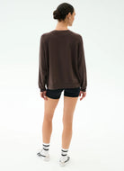 Person wearing a brown sweatshirt and black shorts on a white background