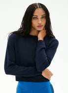 A woman modeling a dark navy blue long-sleeve crewneck top, paired with bright blue athletic bottoms, against a clean white studio background.