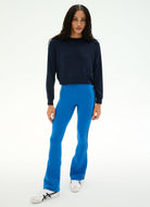 A model wearing a dark navy crewneck sweatshirt, bright blue flared pants, and white sneakers, standing against a plain white studio background.