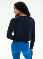 A woman shown from the back wearing a dark navy long-sleeve cropped sweatshirt and bright blue leggings against a clean white studio background.