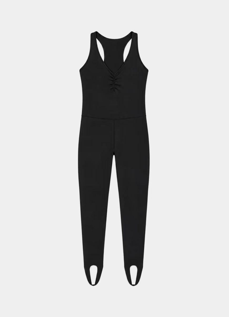 A black sleeveless one-piece jumpsuit with a racerback design, front lace-up detail, and integrated leg warmers with cutout details at the toes, shown against a light gray background.