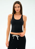 Woman wearing a black tank top and black pants with white drawstrings on a light gray background