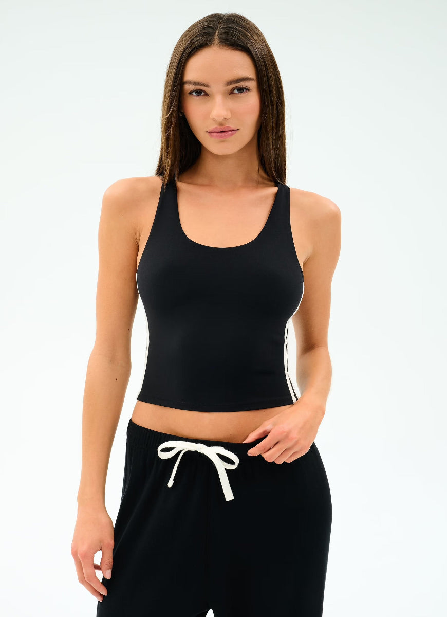 Woman wearing a black tank top and black pants with white drawstrings on a light gray background