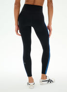 Black high-waisted leggings with a bright blue side stripe and a small white logo near the ankle, shown on a model from the back against a white studio background.