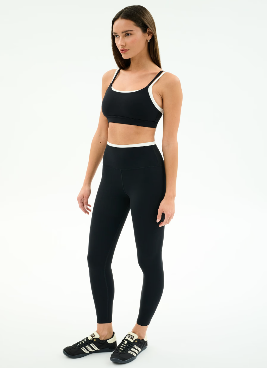 Woman wearing a black sports bra and leggings set on a white background