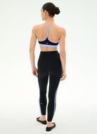 A woman shown from the back wearing a black athletic bra and black leggings with white side stripes, photographed against a clean white studio background.