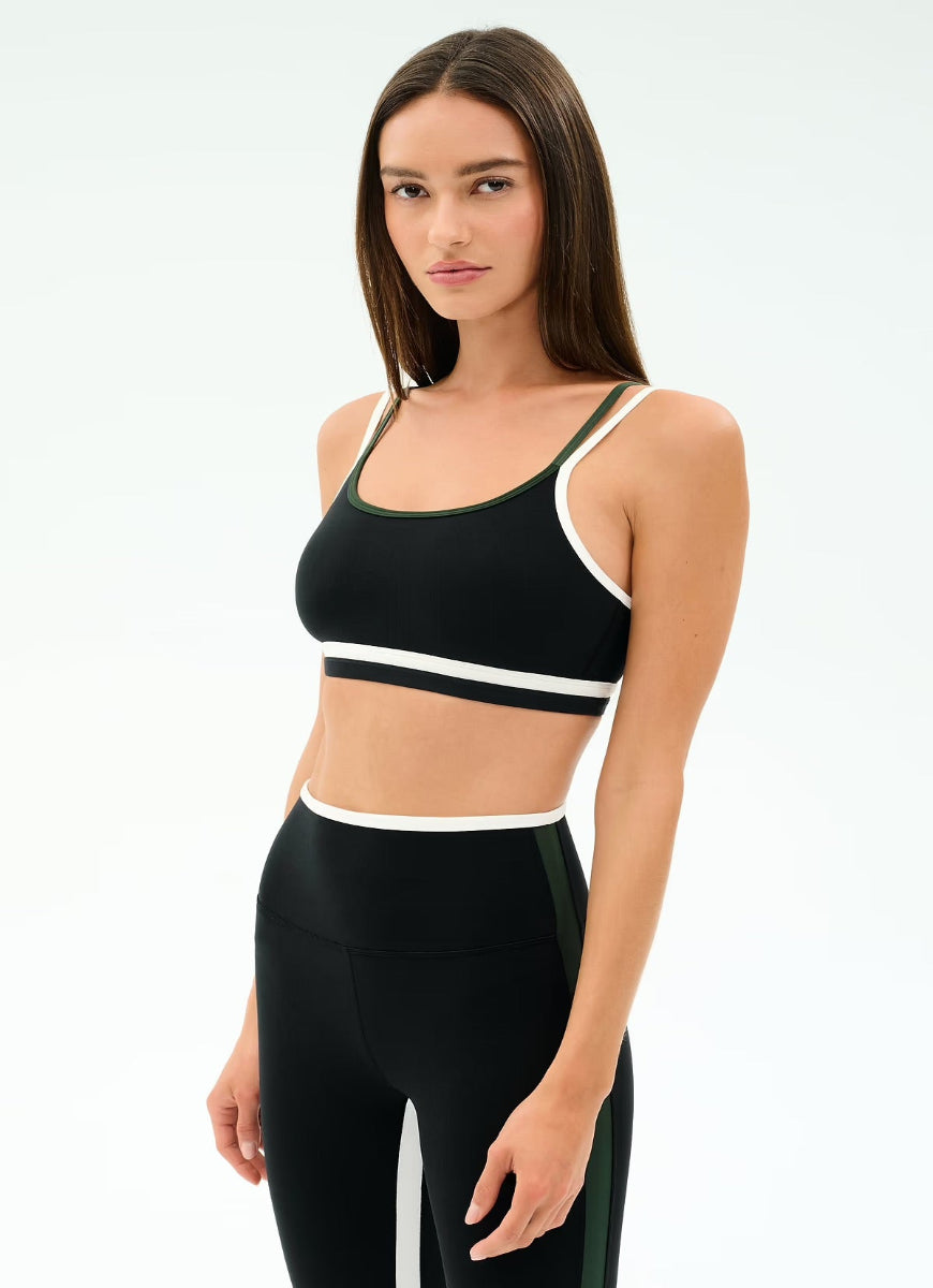 Woman wearing a black sports bra and leggings with white accents on a white background