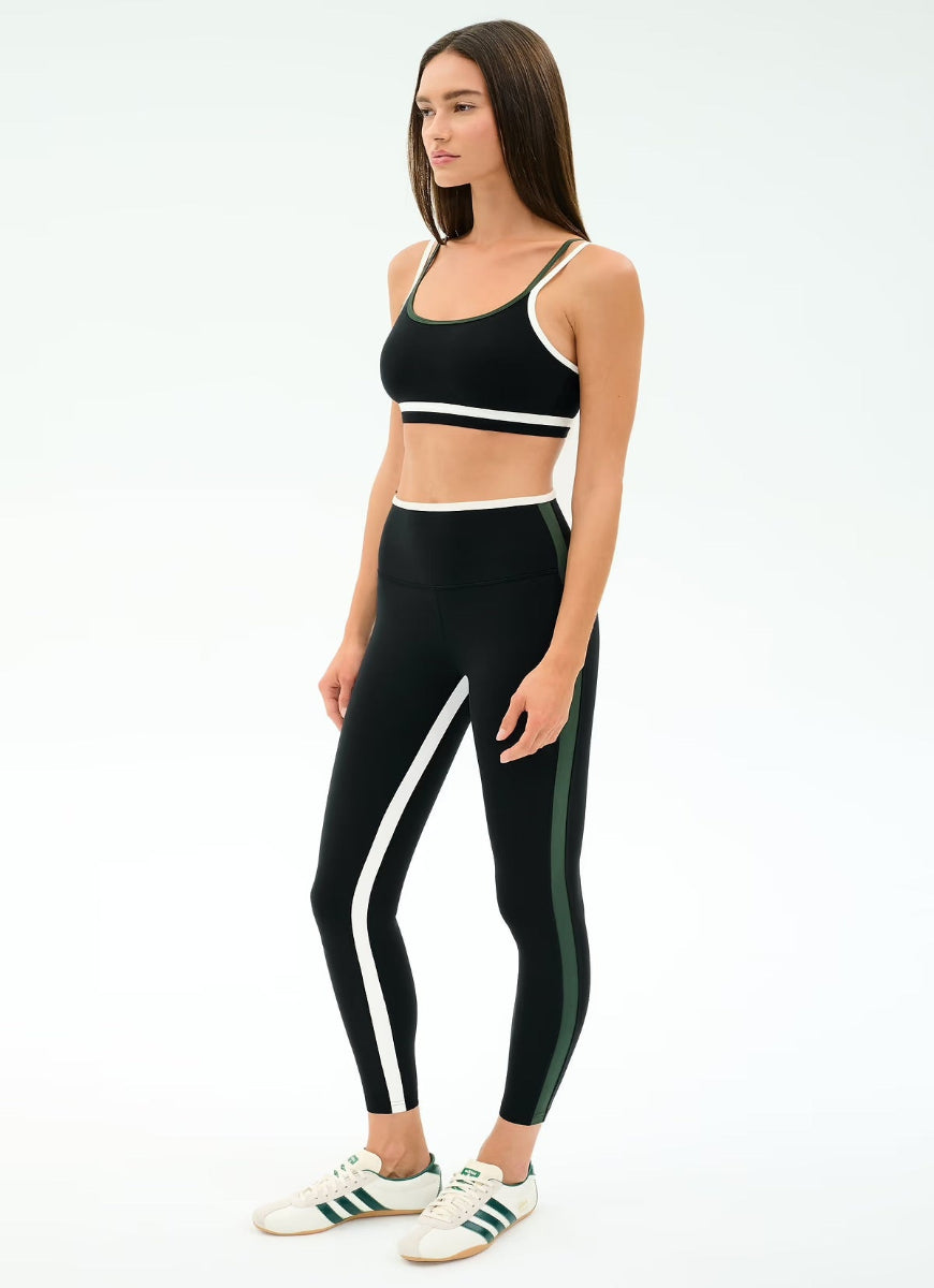Woman wearing a black sports bra and leggings with white stripes on a white background
