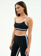 Woman wearing a black sports bra and leggings with blue accents on a white background