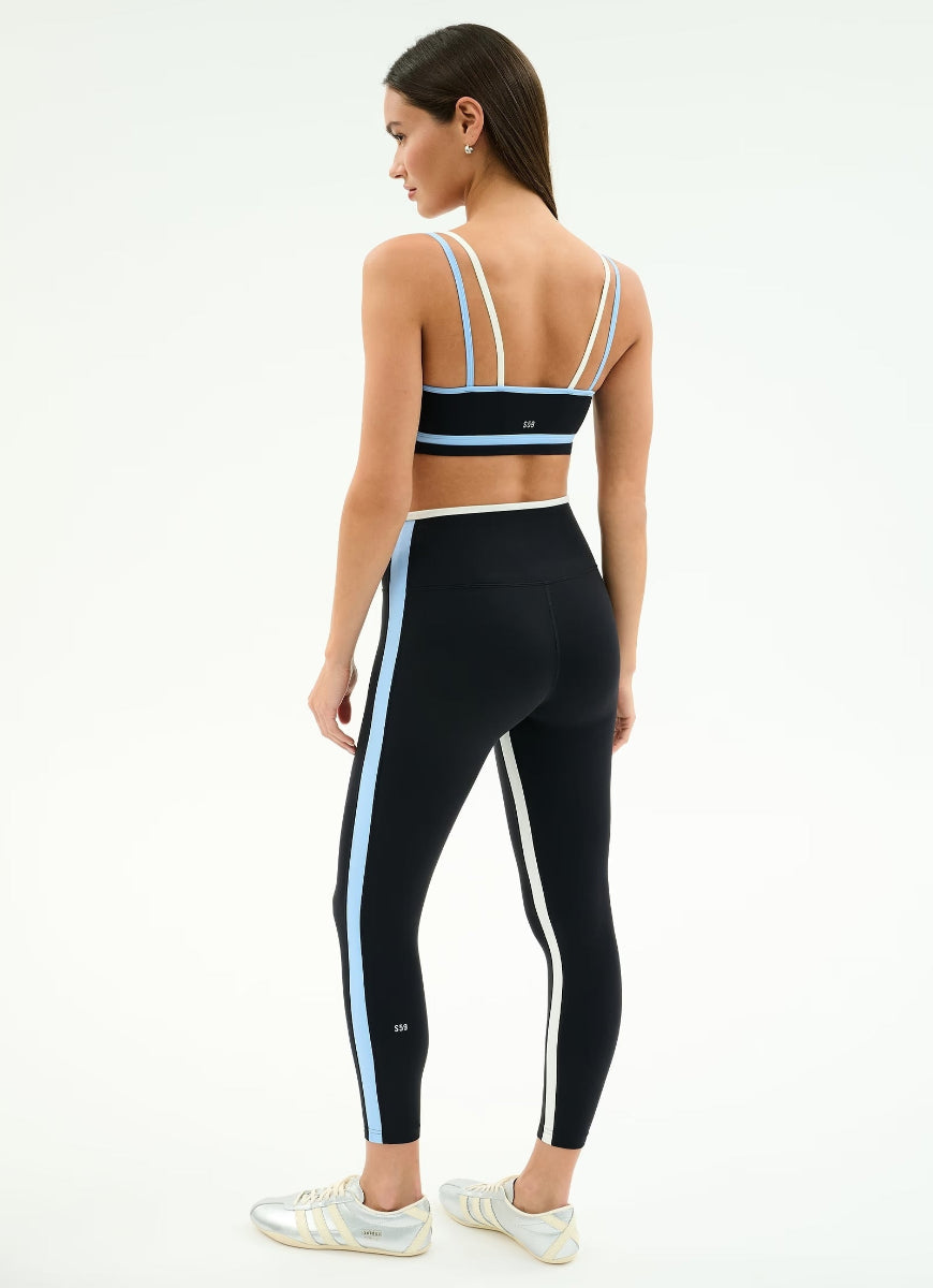 Woman wearing a black sports bra and leggings with blue stripes on a white background