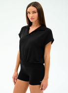 Woman wearing a black polo shirt and black shorts on a white background