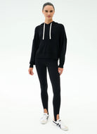 Woman wearing a black hoodie and leggings with white sneakers on a white background