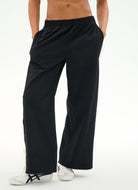 A person wearing black wide-leg athletic pants with white sneakers, shown from the waist down against a clean white studio background.