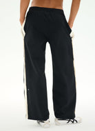Black wide-leg track pants with cream side stripes, shown on a model from the back against a white studio background.