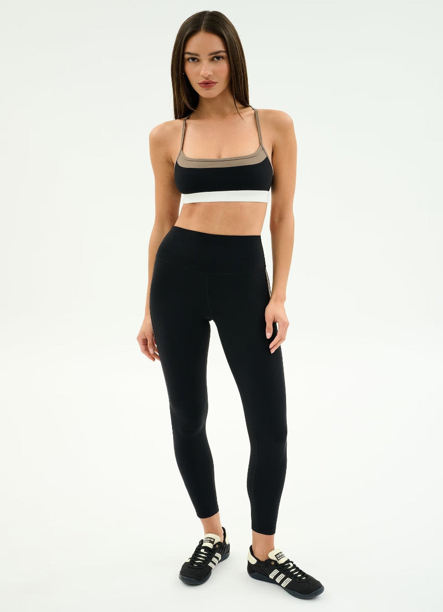 Woman wearing a black sports bra and leggings with white sneakers on a white background