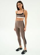 Woman wearing a brown sports bra and leggings with white stripes on a white background