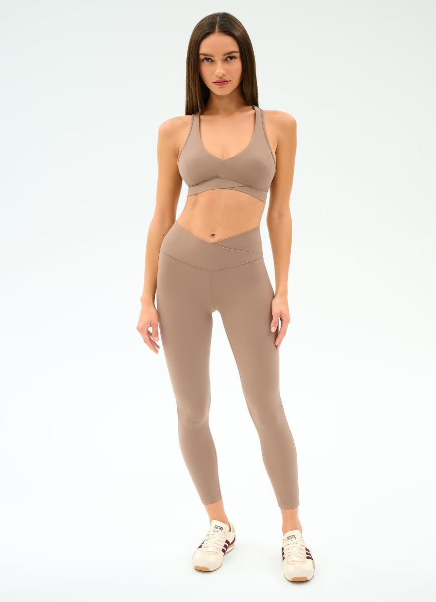 Woman wearing a beige sports bra and leggings set on a white background