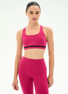 A woman modeling a bright pink activewear set consisting of a sports bra with a black band detail and matching high-waisted leggings, against a plain white studio background.