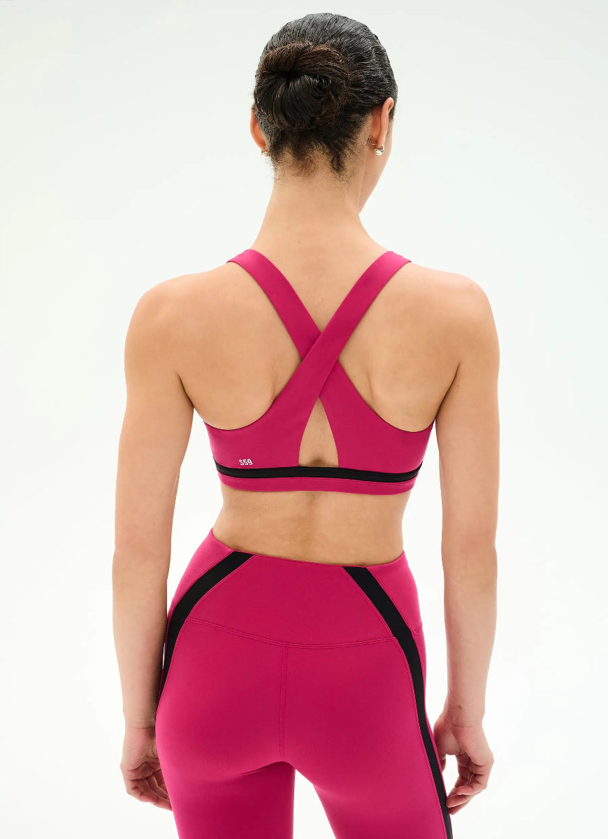 A woman shown from the back wearing a bright pink sports bra and matching high-waisted leggings with black side panels, against a clean white studio background.