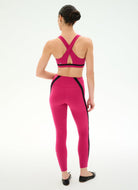 A woman shown from the back wearing a bright pink activewear set consisting of a sports bra with crisscross straps and matching high-waisted leggings with black side panels, photographed against a clean white studio background.
