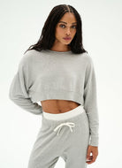 A woman modeling a light gray heather cropped sweatshirt and matching sweatpants with a white drawstring waistband, shot against a plain white studio background.