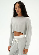 A woman modeling a light gray heather cropped sweatshirt and matching sweatpants set against a plain white studio background.