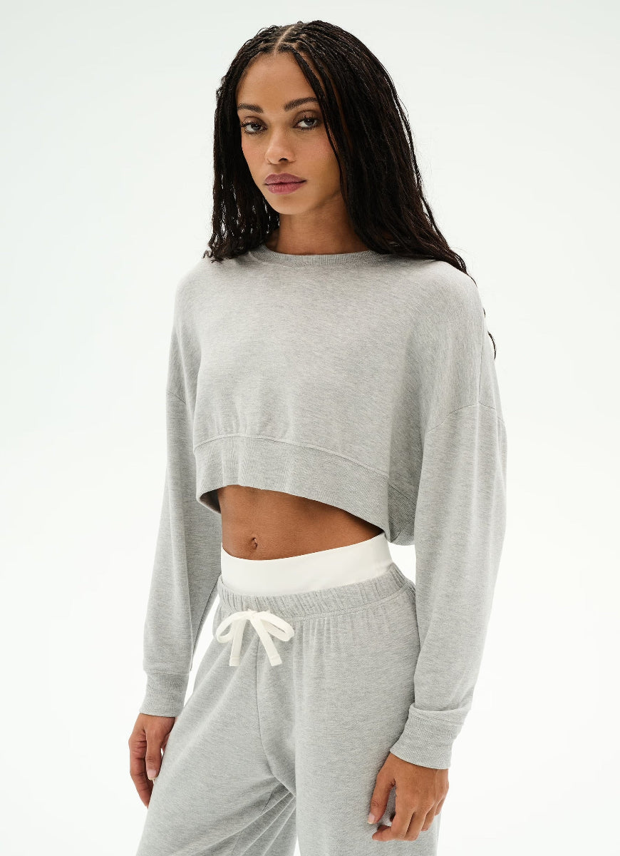 A woman modeling a light gray heather cropped sweatshirt and matching sweatpants set against a plain white studio background.