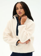 A woman modeling a cream sherpa fleece quarter-zip pullover with a dark navy blue zipper placket and matching dark cuffs, set against a plain white studio background.