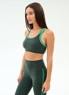 Woman wearing a green sports bra and leggings with white trim on a white background
