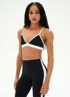 A woman modeling a black and white athletic set consisting of a crossover sports bra and matching high-waisted leggings with white side panels, shot against a plain white studio background.