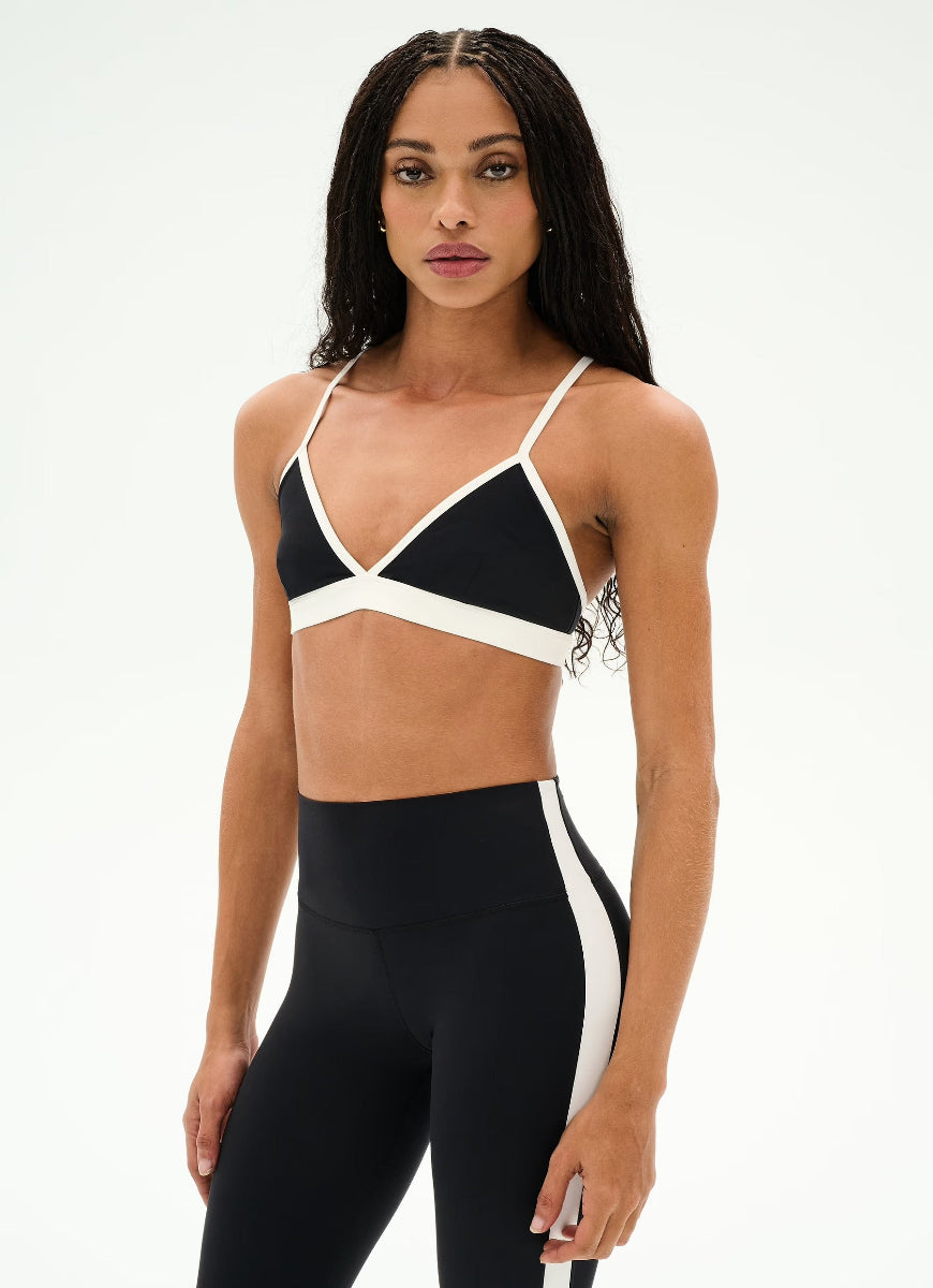 A woman modeling a black and white athletic set consisting of a crossover sports bra and matching high-waisted leggings with white side panels, shot against a plain white studio background.