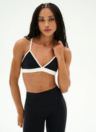 A woman modeling a black and white color-blocked sports bra and black high-waisted leggings against a plain white studio background.
