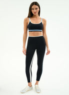 Woman wearing a black sports bra and leggings with white stripes on a white background