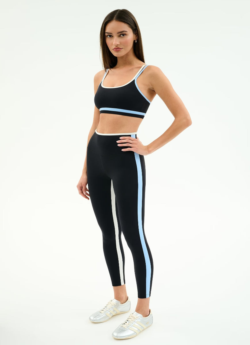 Woman wearing a black sports bra and leggings with white stripes on a white background
