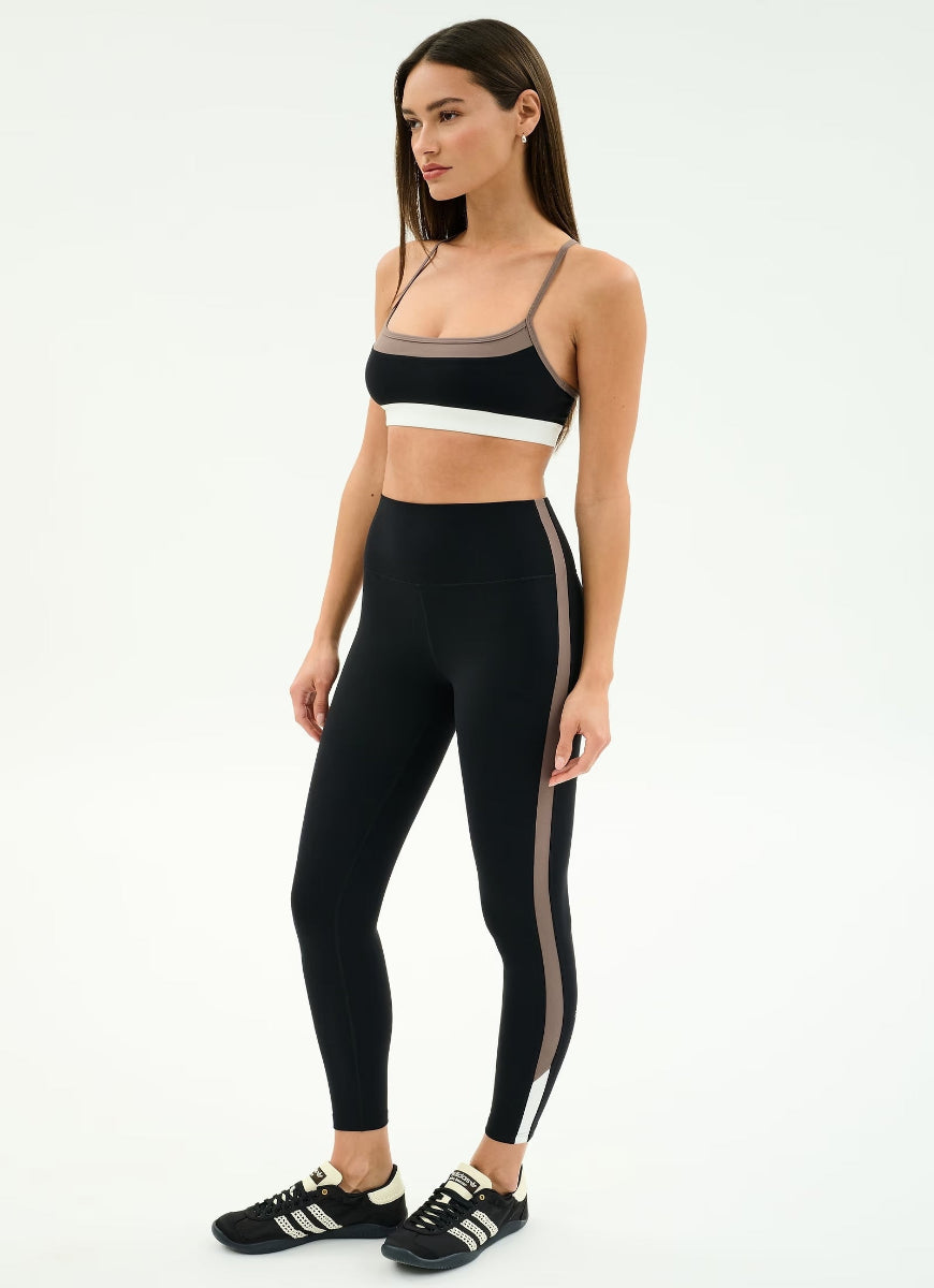 Woman wearing a black athletic outfit with white stripes on a white background